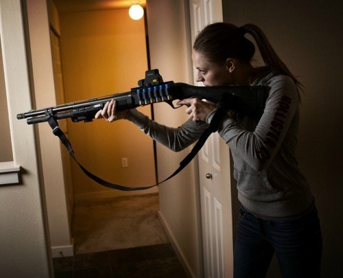 woman holding a shotgun at the ready in a hallway