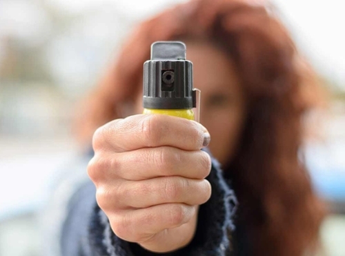 woman with red hair holding a pepper spray pointed at camera